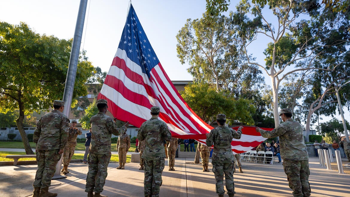 A group of people in military uniforms perform a raising of the American flag ceremony.