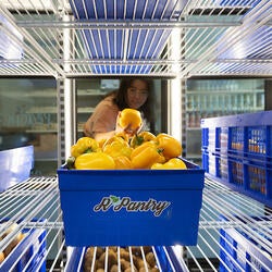 A student looks into the refrigerator to grab an orange from a blue bin labeled R'Pantry